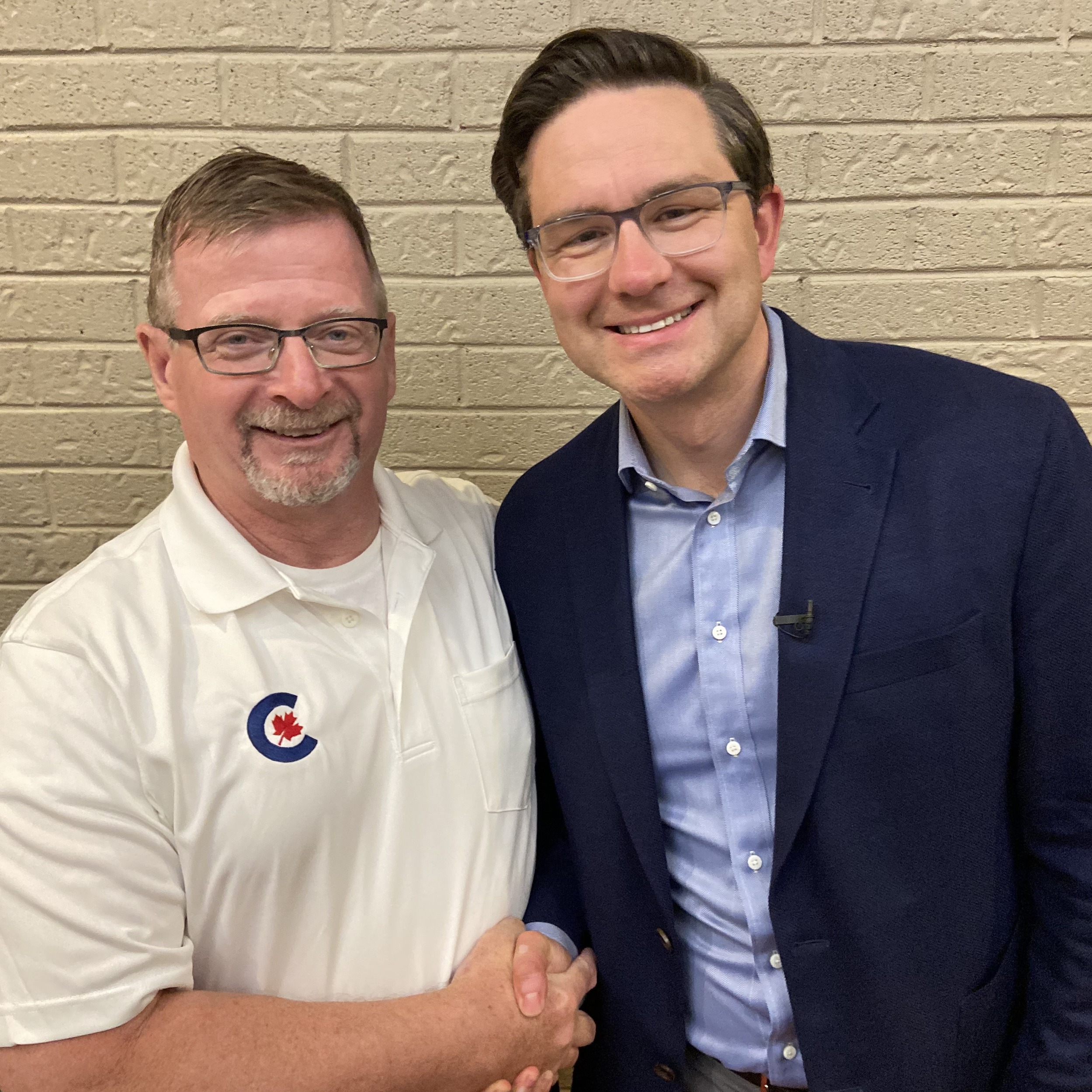 Stephen gallant smiling while shaking hands with smiling Pierre Poilievre