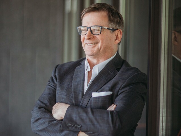 Stephen Gallant in a suit smiling with arms crossed